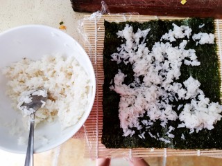 3、肉松寿司,米饭（家里没有东北米了，但是用东北米会更好吃）煮熟后取小碗半碗（两卷寿司的量），倒入适量寿司醋，小半瓶就行，因为倒太多会有点酸，拌匀，然后待它放凉，寿司帘上卷一层保鲜膜，放上一张海苔，在海苔上铺一层刚才拌好的米饭（亲测，米饭一定不要铺多了，不然做出来的寿司卷起来一大卷不好吃也不好卷），米饭看图片上的量就可以了，稍微铺均匀一点