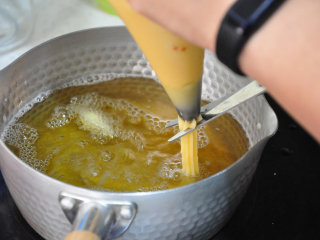 12、西班牙油条——吉拿果,从裱花袋挤出约10cm长的面糊,再用剪刀剪断,让面糊掉入油锅中。