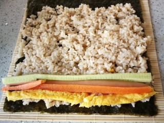 8、紫菜包饭,将切好的鸡蛋条,胡萝卜条,黄瓜条和火腿条均匀摆放在紫菜边缘部分。