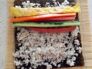 3、紫菜包饭,在紫菜上铺上米饭 边缘留一点不要放米饭 尽力铺的厚薄一致 放上黄瓜条 火腿肠的条 蛋皮条 胡萝卜条 ...