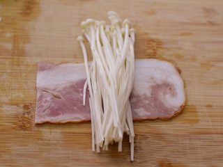 4、金针菇培根卷,取一半,放些金针菇在上面。