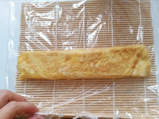 16、秋葵厚蛋烧,自己吃可以直接切成段了。如果招待客人或者想要成品更完美，准备寿司帘，上面铺上一层保鲜膜，放上厚蛋烧，卷起来，压紧实，定型