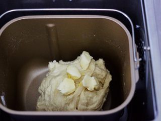 4、椰蓉奶香面包圈,和面第1阶段结束后，面团处于扩展阶段，这时加入室温软化的黄油，继续一个和面程序。