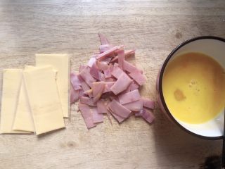 1、爆浆鸡蛋卷,芝士一片切成两片，火腿片切小条，鸡蛋打散。