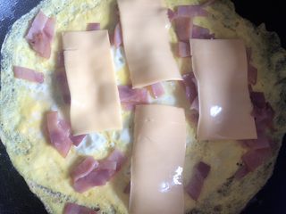 2、爆浆鸡蛋卷,油锅下鸡蛋液，铺成饼状，开小火，放入火腿小条，铺上芝士片。