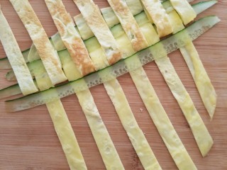 5、菠萝蛋包饭,把鸡蛋条和黄瓜条按照编花篮的方法编成蛋饼，如图每隔一个把鸡蛋条揭起放入黄瓜条。看到揭开蛋条贴着锅底的颜色了吧，这就是为什么煎蛋饼时不要翻面，要保证表面颜色漂亮，翻面贴到锅底就会有斑纹。