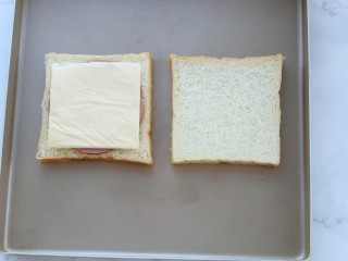 2、沼夫三明治,将土司片放进烤盘内，在其中一片土司上放火腿和芝士，放进170度预热好的烤箱中层上下火烤五分钟取出