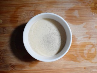 2、奶香葡萄干小面包（电饭锅版）,在牛奶中倒入4g酵母粉，并用筷子搅拌至融化。