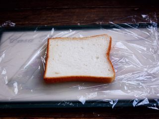 3、三明治,做三明治时先在粘板上铺上一大块保鲜膜,然后放上一片吐司面包。