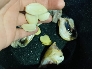 8、砂锅鱼头煲,待鱼头稍微变黄，即可将蒜头和姜片加入锅里一起煎；