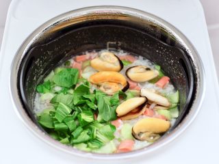 12、青口火腿青菜粥,再打开锅盖加入焯过水的青口和青菜叶。