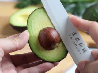 2、绿色美食+烟熏三文鱼牛油果沙拉,刀卡住果核，一手拿住牛油果，一手握住刀柄左右转动，取出果核，操作如图。