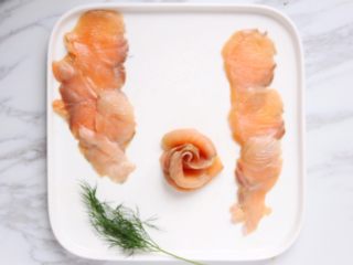 8、绿色美食+烟熏三文鱼牛油果沙拉,如图三片依次叠好，卷起来就成花的形状了（五片鱼卷起来更好看），花边向外翻翻，放到沙拉盘中。