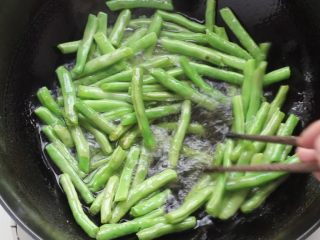 5、干煸豆角,锅中稍多些的油，七成热放入豆角剪炸，炸至豆角表面起泡，捞出沥油。