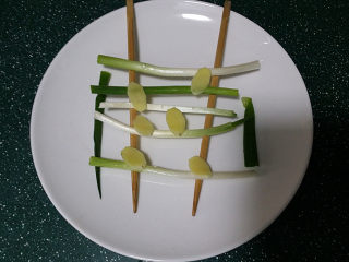 4、剁椒鱼头,取一大盘子上面架起一双筷子、放上洗净的葱段和姜片，也是达到去腥增香的作用