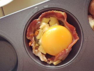 9、小芽早餐-培根鸡蛋彩蔬玛芬,向每个玛芬杯中打入一个鸡蛋。然后放入预热好的烤箱中，180度，烤制8-10分钟（想要鸡蛋熟一点就多烤几分钟，但不要烤太久，不然鸡蛋外层会有一层干皮，口感不好）