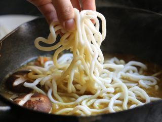 11、海鲜咖喱乌冬面,加入乌冬面和香菇，中小火煮，期间用锅铲不时翻拌一下。