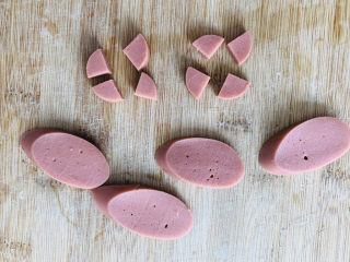 10、烤馒头片,准备一根火腿肠去掉外皮先切几个小圆片,圆片从中间一分为四,用来做猪耳朵,然后再斜着切出几个椭圆形的薄片用来做猪鼻子。