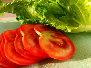 4、鸡胸肉三明治,清洗好的西红柿切成薄片,生菜清洗干净,因为西红柿个和生菜都是生吃,所以在清洗的时候要额外的主意,先清洗两遍之后用淡盐水浸泡15分钟,最后再冲洗干净。