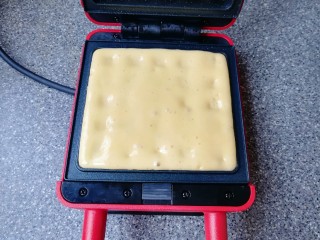 6、早餐华夫饼,预热好的华夫饼早餐机烤盘里倒入准备好的华夫饼面糊，盖上盖子加热4-5分钟。