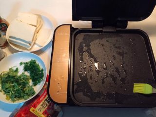1、铁板豆腐,煎烤机预热3分钟，然后刷油。