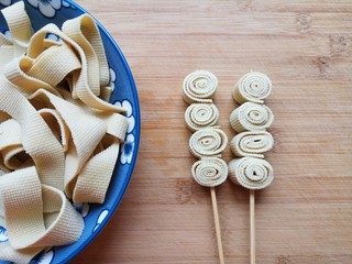 1、关东煮,豆腐皮冲洗一下煮熟，切成条状，卷起来穿成串。 