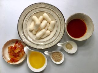 1、韩式年糕,准备好年糕、韩式辣酱、韩国泡菜、菜籽油、胡椒粉、白芝麻等所有食材。年糕选择蛋黄馅年糕口感好点，白芝麻微波炉叮熟，韩国泡菜切成片。