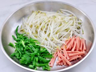 15、超过瘾好吃的酸辣银丝,把焯熟的绿豆芽和青椒丝，火腿丝放入大一点的容器中。