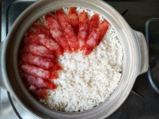 11、腊味煲仔饭,再将腊味铺在米上，因为这样腊肠的咸度会更低一些，然后再煮5分钟，在煲煮的过程中，米饭会自动吸收腊味的精华，米饭被肉香包裹，才是煲仔饭的正道。