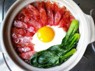 13、腊味煲仔饭,然后在饭上磕上一个鸡蛋，摆上焯熟的油菜，再焖2-3分钟。