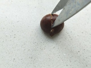 4、糖烤板栗,拿一个板栗，用剪刀竖着把板栗剪开口。