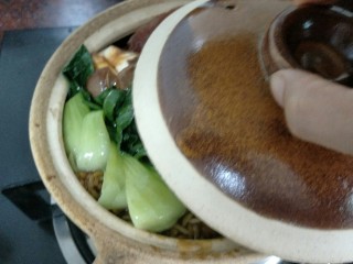 11、腊肠煲仔饭,把青菜放上去,盖上砂锅盖小火煮大概1分钟后熄火