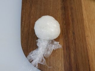 4、卡通大白饭团便当盒,用保鲜膜包裹住捏成圆形，捏好不要拆开保鲜膜，直接放到一旁定型备用