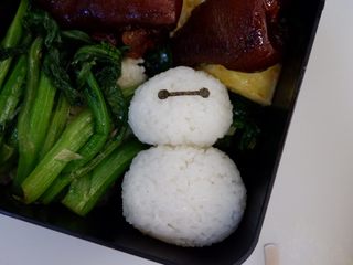 11、卡通大白饭团便当盒,最后用镊子把海苔表情粘上去就完成了。如果饭团不够粘，可以涂抹少许沙拉酱