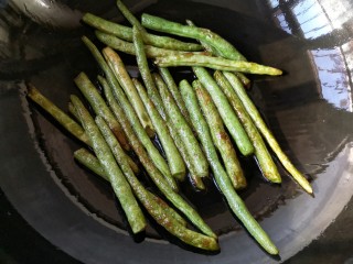 8、干煸芸豆,锅中适量油（30克左右，不用太多）烧热，把沥干水的芸豆入锅，中小火不断翻炒，至芸豆表皮皱褶微焦后沥油盛出备用。