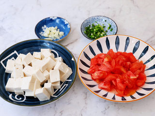 2、番茄烧豆腐,番茄洗净底部切十字，放入开水中焯烫，烫至皮翘取出去皮，然后切成小块备用，豆腐切成小块，蒜切末，葱切葱花