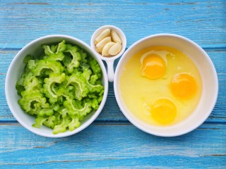 1、苦瓜炒蛋,准备好所有食材。苦瓜洗净后将里面的瓤掏干净切片，取3个鸡蛋打散搅拌均匀放在碗中备用。 大蒜去皮拍扁。