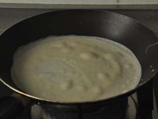 5、做饼+法式鲜虾芦笋烘饼,舀一勺面糊到锅里，轻轻摇晃锅子使面糊迅速摊开。