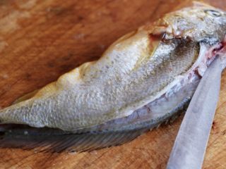 3、清蒸剁椒黄花鱼,把黄花鱼放在菜板上、用刀先在黄花鱼的头部开始片刀到黄花鱼的鱼尾处、切记不要把黄花鱼的肚子切开呀