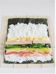 10、紫菜包饭,再靠近自己的这一边，依照自己的喜好在米饭上放上煎蛋、火腿、菠菜、腌萝卜和蟹棒，挤上一些沙拉酱，撒一些芝麻