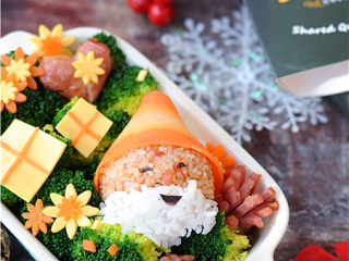 11、圣诞老人便当,西红柿饭团上面裹上胡萝卜片做帽子，紫菜片点缀成眼睛嘴巴，粘上白米饭做胡须，圣诞老人饭团就做好了，周围摆上西兰花、胡萝卜花、芝士片装饰下就可以了。