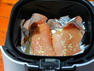 8、香蒜蜂蜜烤鸡胸,空气炸锅的炸篮里铺一张锡纸，把腌制好的鸡胸肉放到里面。