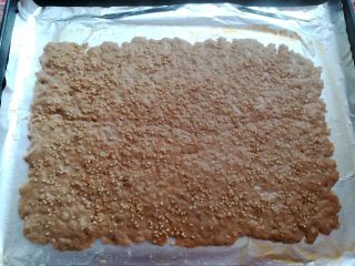 14、自制猪肉脯,烤到肉沫大量出水后取出烤盘,用另外一只手戴上一次性手套扶住肉饼,倒掉多余的水份,放回烤箱继续烤,烤到表面上色后取出,给肉饼翻面刷蜂蜜水撒芝麻