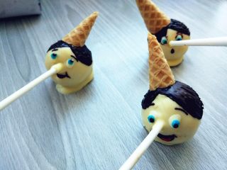 12、皮诺曹棒棒糖蛋糕,将少许白巧克力中调入少许蓝色和红色色素，画出蓝眼睛和嘴巴。