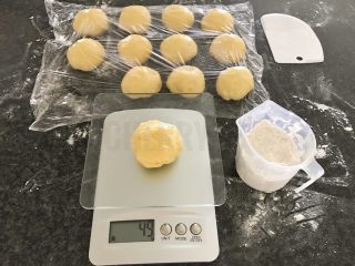 12、#家有烤箱#黑芝麻豆沙面包,在面板上，撒些干粉，我们先将面团分成12份，每分50g左右，盖上保鲜膜再醒发10分钟，