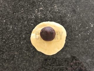 14、#家有烤箱#黑芝麻豆沙面包,将醒发好的面团，用擀面杖擀成圆形，上面加一颗豆沙丸子，