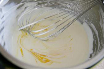 4、轻乳酪杯子蛋糕,奶酪糊里分次加入三个蛋黄拌匀后，边缓缓加入黄油边用手动打蛋器拌匀。