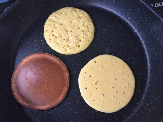 3、软软奶香玉米饼,平底锅预热，不要放油～舀一勺面糊倒在平底锅中，它会自然摊开变成圆形。最上面那个起泡泡的状态就可以翻面了，火可以小一点，我刚开始火大了翻面不及时就会像下面那个上色太重了。