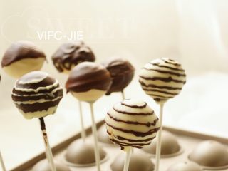 21、巧克力棒棒糖蛋糕,剩余的黑巧克力装入裱花袋里，底下剪一个小小的口，然后在白巧克力棒棒糖蛋糕上做一些装饰，画一些圈圈即可