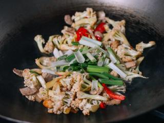 7、干锅花菜,接下来，加入花菜 和红椒。炒1分钟。添加半勺盐、1勺生抽、1勺绍兴黄酒,1勺香油,半勺白胡椒粉,1勺蚝油,少许水。翻炒，盖上盖子，煮1- 2分钟。开盖再加入葱翻炒一下。